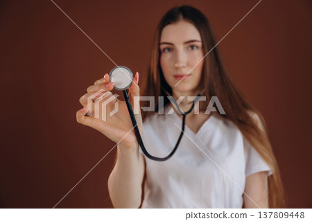 Holding the stethoscope. Female doctor is in the studio Holding the stethoscope. Female doctor is in the studio 137809448