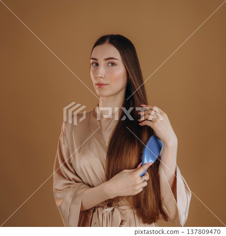 Combs her hair, brushing. Young woman is against background Combs her hair, brushing. Young woman is against background 137809470