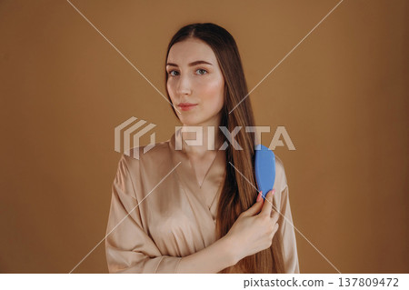 Combs her hair, brushing. Young woman is against background Combs her hair, brushing. Young woman is against background 137809472
