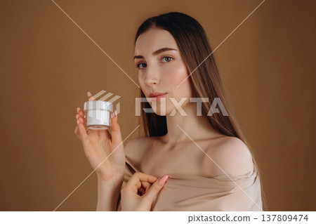 Advertisement for the facial cream. Young woman is against background 137809474