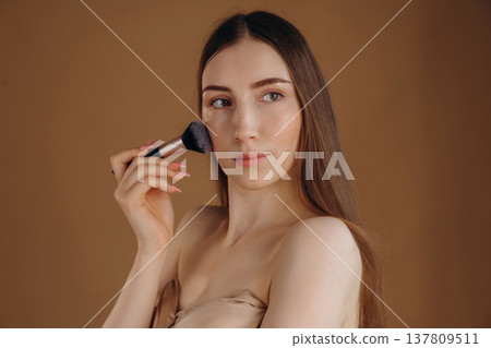 Using brush, cosmetics on face. Young woman is against background 137809511