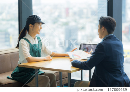 A man in a suit is having a meeting with a woman working at a cafe. A man in a suit is having a meeting with a woman working at a cafe. 137809689