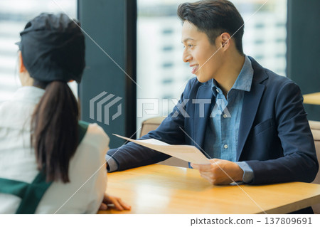 A man in a suit is having a meeting with a woman working at a cafe. A man in a suit is having a meeting with a woman working at a cafe. 137809691