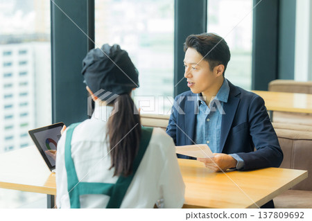 一名身穿西裝的男子正在與一名在咖啡館工作的女子會面。 137809692
