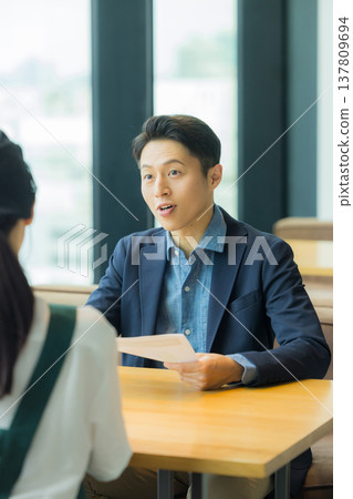 A man in a suit is having a meeting with a woman working at a cafe. 137809694