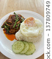 Thai food stir fry curry rice fried egg cucumber lunch dinner spicy homemade Thai food stir fry curry with rice fried egg cucumber lunch dinner spicy comfort meal on white plate wooden table 137809749