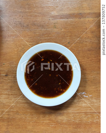 Soy sauce dipping sauce asian food brown liquid white bowl wooden table salty flavor traditional recipe closeup overhead view savory condiment adds rich depth to simple meal presentation Soy sauce dipping sauce asian food brown liquid white bowl wooden table salty flavor traditional recipe closeup overhead view savory condiment adds rich depth to simple meal presentation 137809752