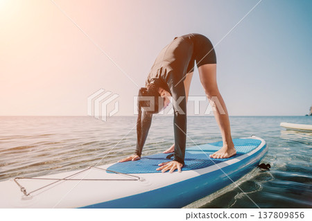 Yoga Paddleboard Woman Beach - Woman doing yoga on paddleboard at beach during sunset. Yoga Paddleboard Woman Beach - Woman doing yoga on paddleboard at beach during sunset. 137809856