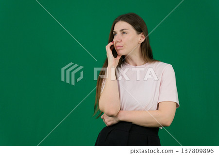 Various emotions of a European woman in a pink T-shirt and black pants on a green background with long brown hair in different poses Various emotions of a European woman in a pink T-shirt and black pants on a green background with long brown hair in different poses 137809896
