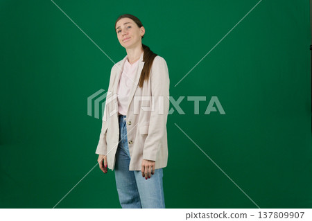 Various emotions and poses of a woman in a beige jacket and jeans, wearing a pink European T-shirt with her hair pulled back into a ponytail, against a green background 137809907