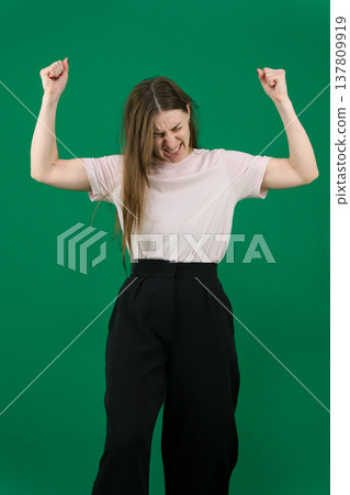 Various emotions of a European woman in a pink T-shirt and black pants on a green background with long brown hair in different poses 137809919