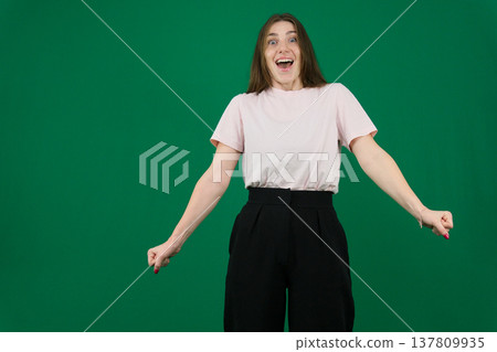 Various emotions of a European woman in a pink T-shirt and black pants on a green background with long brown hair in different poses Various emotions of a European woman in a pink T-shirt and black pants on a green background with long brown hair in different poses 137809935