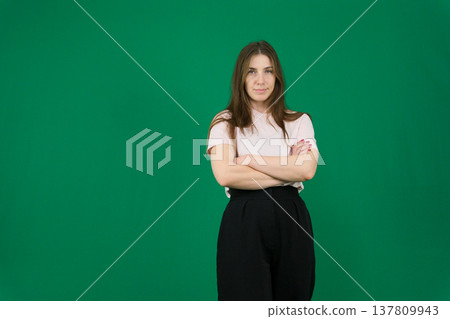 Various emotions of a European woman in a pink T-shirt and black pants on a green background with long brown hair in different poses 137809943