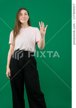 Various emotions of a European woman in a pink T-shirt and black pants on a green background with long brown hair in different poses 137809957
