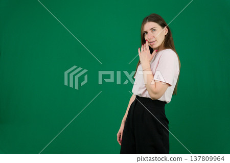 Various emotions of a European woman in a pink T-shirt and black pants on a green background with long brown hair in different poses 137809964