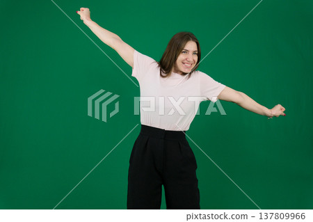 Various emotions of a European woman in a pink T-shirt and black pants on a green background with long brown hair in different poses Various emotions of a European woman in a pink T-shirt and black pants on a green background with long brown hair in different poses 137809966