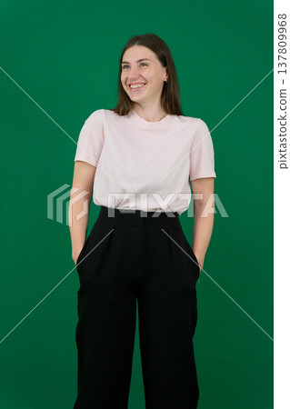 Various emotions of a European woman in a pink T-shirt and black pants on a green background with long brown hair in different poses 137809968