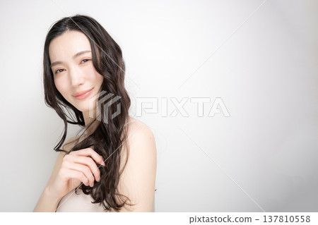 一位留著黑色長捲髮的女子,頭髮在白色背景的映襯下飄逸動人;她直視鏡頭,這張照片旨在宣傳護髮和護理產品。 一位留著黑色長捲髮的女子,頭髮在白色背景的映襯下飄逸動人;她直視鏡頭,這張照片旨在宣傳護髮和護理產品。 137810558