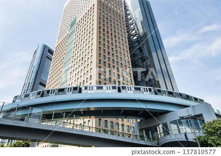 Low-angle view of a New Transit Yurikamome line train running on the elevated track with modern skyscrapers in Shiodome, Minato, Tokyo, Japan. It's an automated guideway transit service in Tokyo. Low-angle view of a New Transit Yurikamome line train running on the elevated track with modern skyscrapers in Shiodome, Minato, Tokyo, Japan. It's an automated guideway transit service in Tokyo. 137810577