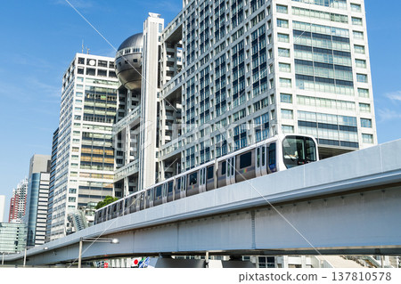 View of a New Transit Yurikamome line train running on the elevated track, driving past the Fuji Television building in Koto, Tokyo, Japan. It's an automated guideway transit service in Tokyo. View of a New Transit Yurikamome line train running on the elevated track, driving past the Fuji Television building in Koto, Tokyo, Japan. It's an automated guideway transit service in Tokyo. 137810578