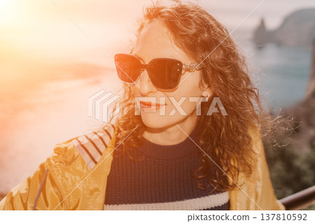 Woman sunset ocean happy traveler in yellow jacket wearing sunglasses enjoys the view overlooking a calm coastal bay 137810592