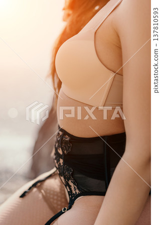 Lingerie bra woman wearing beige undergarments and black lace garter belt with stockings outdoors in soft sunlight 137810593