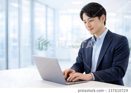 一名男性上班族在站立式辦公桌前使用筆記型電腦工作。 137810729