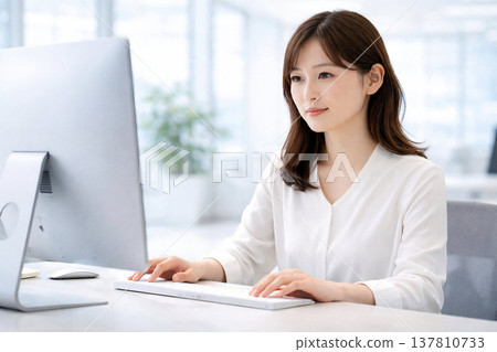 Female office worker performing data analysis on desktop monitor 137810733