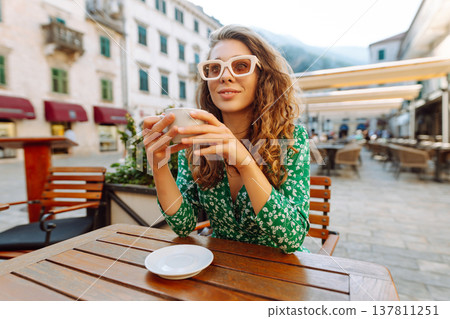 Happy woman sitting by table drinking coffee of outdoor sidewalk cafe restaurant, on summer day. 137811251