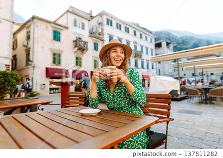 Happy woman sitting by table drinking coffee of outdoor sidewalk cafe restaurant, on summer day. 137811282