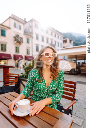 Happy woman sitting by table drinking coffee of outdoor sidewalk cafe restaurant, on summer day. 137811283