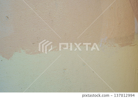 A horizontal close-up shot of a textured concrete wall painted in two tones of beige and light yellow. 137812994