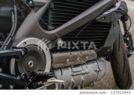 A detailed horizontal shot of the lower section of an electric motorcycle, showing the textured battery casing, cooling fins, and silver-colored motor housing integrated into a dark frame. 137813443