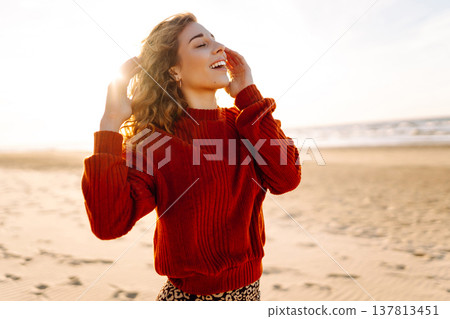 Portrait of a beautiful woman on the beach at sunset. Girl walks along the beach and enjoys weather 137813451