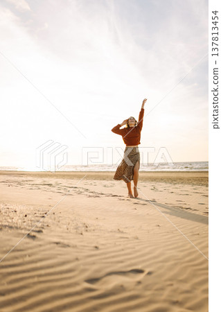 Beautiful woman on the beach in cold weather enjoying time in the sunset. Lifestyle, adventure. 137813454