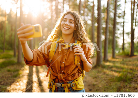 Selfie in nature. Beautiful woman taking picture of herself while walking in a sunny forest. Selfie in nature. Beautiful woman taking picture of herself while walking in a sunny forest. 137813606