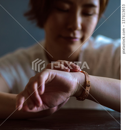 The woman looks at the bracelet on her wrist. The woman looks at the bracelet on her wrist. 137813653