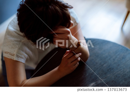 一位女士倚在桌上，低頭看著自己的手腕。 137813673