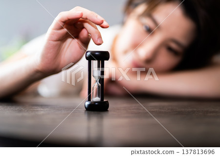 A woman gazes at an hourglass. A woman gazes at an hourglass. 137813696