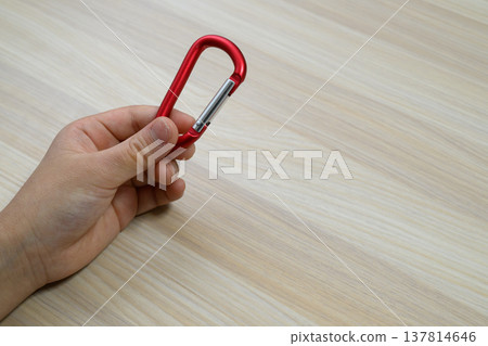 A red carabiner held in the hand against a wide background. 137814646