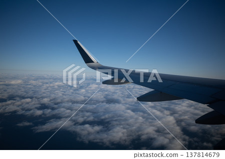 The wings of an aircraft flying over a vast sea of clouds and a blue sky, as seen from the window of an airplane. The wings of an aircraft flying over a vast sea of clouds and a blue sky, as seen from the window of an airplane. 137814679