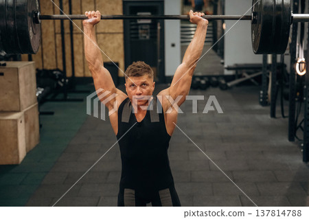 Strong arms and back. Athletic man performing weightlifting exercises with a barbell in a gym Strong arms and back. Athletic man performing weightlifting exercises with a barbell in a gym 137814788