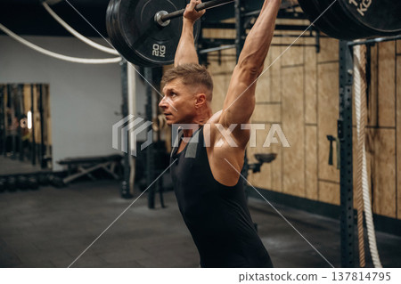 Professional occupation. Athletic man performing weightlifting exercises with a barbell in a gym 137814795