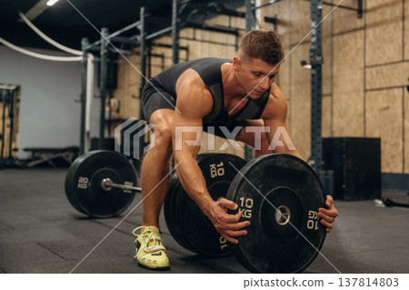 Adding more weight. Athletic man performing weightlifting exercises with a barbell in a gym Adding more weight. Athletic man performing weightlifting exercises with a barbell in a gym 137814803