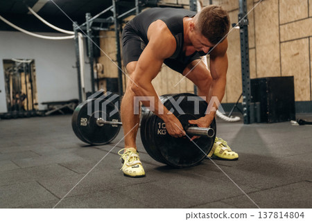 Adding more weight. Athletic man performing weightlifting exercises with a barbell in a gym Adding more weight. Athletic man performing weightlifting exercises with a barbell in a gym 137814804