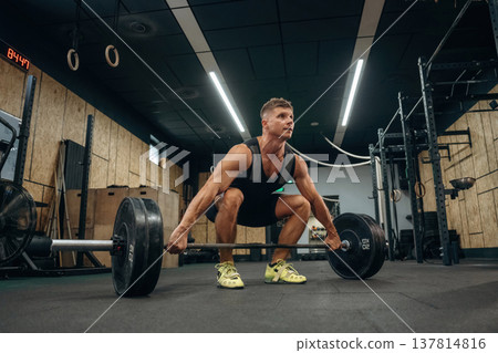 Conception of weightlifting. Athletic man is doing exercise with a barbell in a gym 137814816