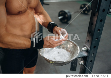 Preparing for competition. Fitness man is rubbing his hands with chalk, specifically magnesium carbonate Preparing for competition. Fitness man is rubbing his hands with chalk, specifically magnesium carbonate 137814861