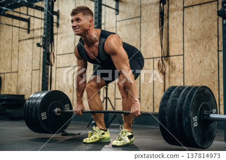 Preparing to do this. Athletic man performing weightlifting exercises with a barbell in a gym Preparing to do this. Athletic man performing weightlifting exercises with a barbell in a gym 137814973