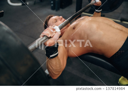 Pushing the barbell, lying down. Athletic man performing weightlifting exercises in a gym Pushing the barbell, lying down. Athletic man performing weightlifting exercises in a gym 137814984