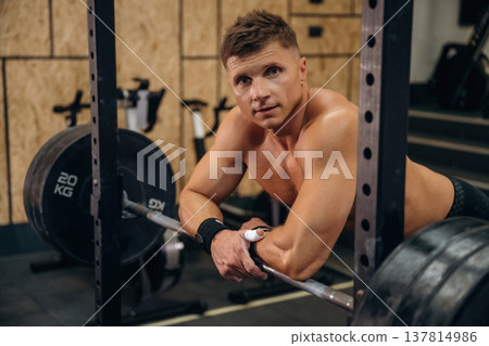 Time for the rest, standing and leaning on the barbell. Athletic man is in a gym Time for the rest, standing and leaning on the barbell. Athletic man is in a gym 137814986